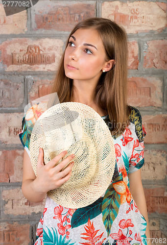 Image of Portrait of pensive girl with a straw hat in hand.