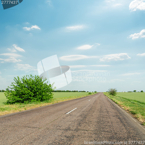 Image of asphalt road in green fields and blue cloudy sky