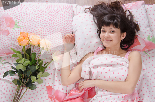 Image of cute girl in bed surprised bestowed a bouquet of roses