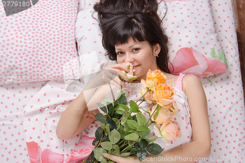 Image of Beautiful girl enjoying scent of flowers in bed