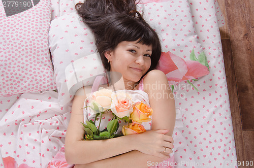 Image of Girl in bed hugged a bouquet of roses