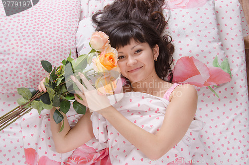 Image of Girl in bed holding a bouquet of roses