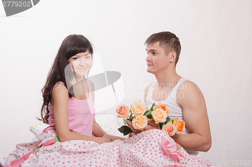 Image of Girl receives flowers from a guy sitting in bed