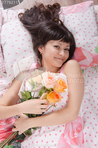 Image of Beautiful young girl lying in bed with bouquet of roses