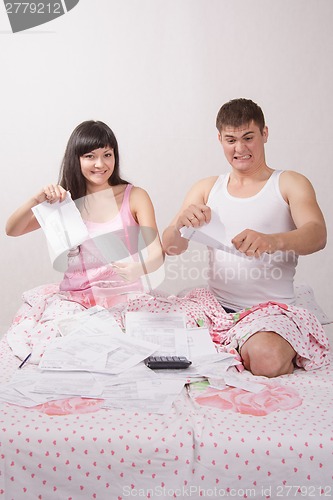 Image of Young family sitting in bed tearing boring invoice