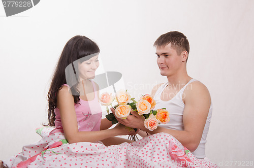 Image of Girl receives flowers from guy sitting in bed