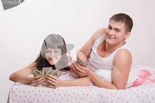 Image of Happy girl and guy with wad of money in bed