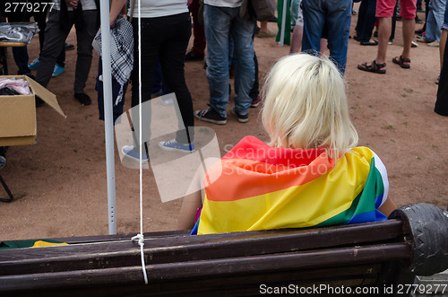 Image of blonde woman sit on bench dressed rainbow gay flag 