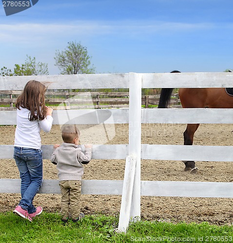 Image of Pre-teen girl and Baby boy on the a white picket fence beside th