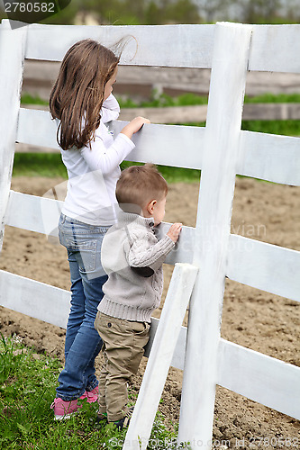 Image of Pre-teen girl and Baby boy on the a white picket fence beside th