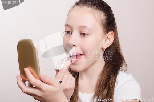 Image of Girl painted lipstick and looks in the mirror