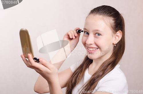 Image of Twelve year old girl paints eyelashes mascara