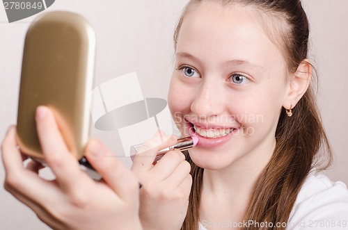 Image of Twelve year old girl paints lips with lipstick