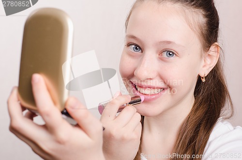 Image of Teen girl paints lips with lipstick