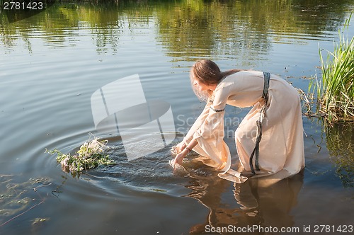 Image of Beautiful girl lowers wreath in water