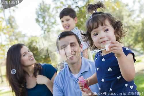Image of Cute Young Baby Girl Blowing Bubbles with Family in Park