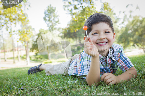 Image of Young Boy Enjoying His Lollipop Outdoors Laying on Grass