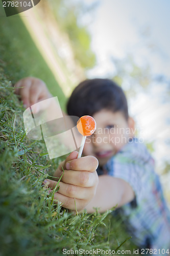 Image of Young Boy Enjoying His Lollipop Outdoors Laying on Grass