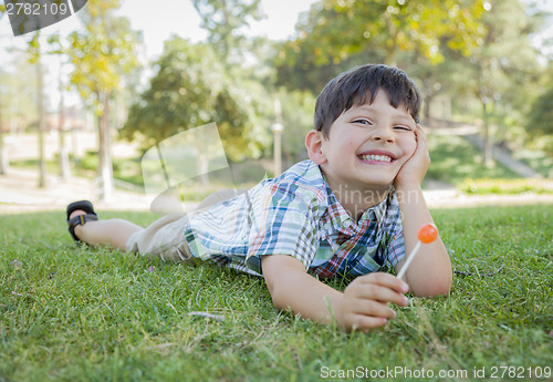 Image of Young Boy Enjoying His Lollipop Outdoors Laying on Grass