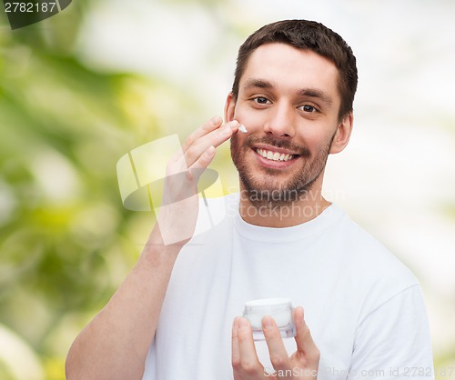 Image of beautiful smiling man applyin cream