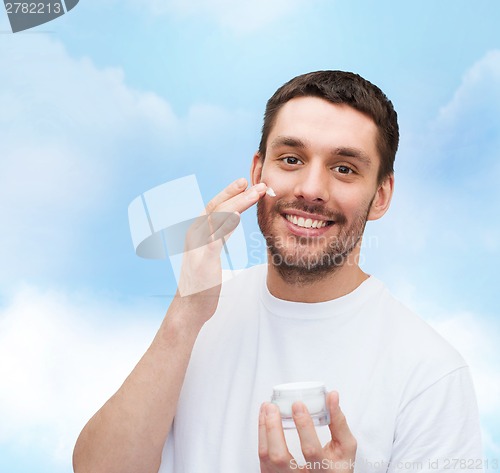 Image of beautiful smiling man applyin cream