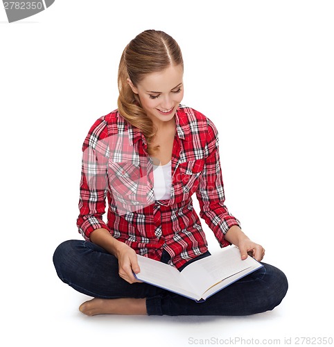 Image of smiling young woman sitting on floor with book