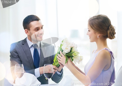 Image of smiling man giving flower bouquet at restaurant