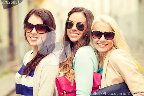 Image of three smiling women in sunglasses with bags
