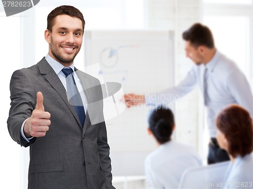 Image of handsome buisnessman showing thumbs up in office
