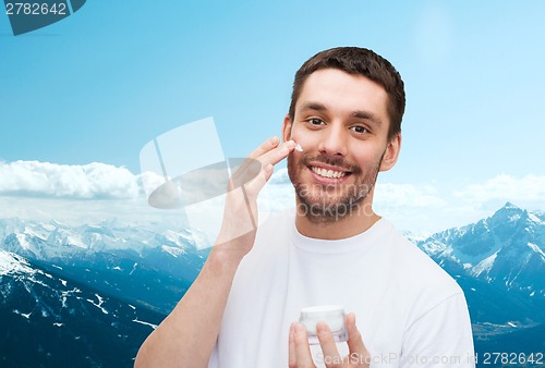Image of beautiful smiling man applyin cream