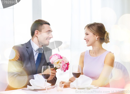 Image of smiling man giving flower bouquet at restaurant