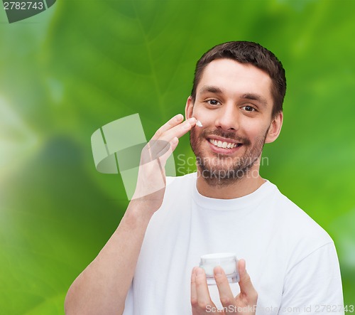 Image of beautiful smiling man applyin cream