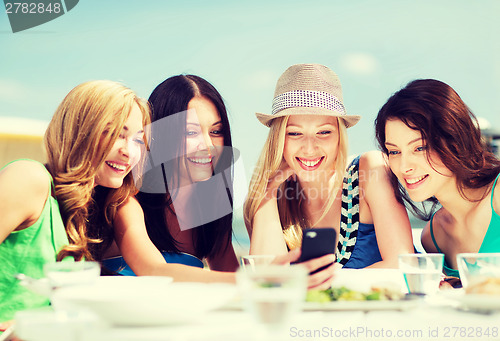 Image of girls looking at smartphone in cafe on the beach