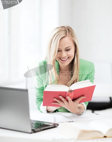 Image of smiling student girl reading book in college