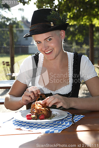 Image of Blonde girl eats half chicken in a traditional beer garden