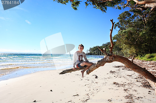 Image of Cheerful teen boy sitting on tree  holiday at the beach Australi