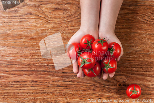 Image of red tomatoes in hands on wooden background