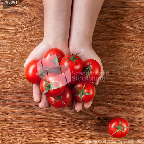 Image of red tomatoes in hands on wood