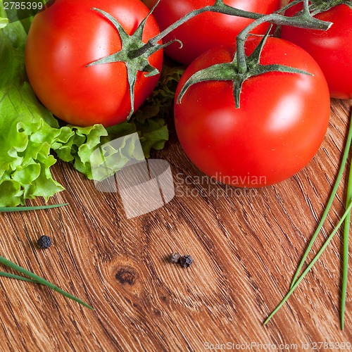 Image of red tomatoes with green salad on wood