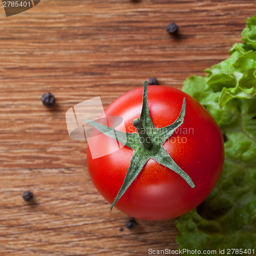 Image of red tomato with green salad on wood