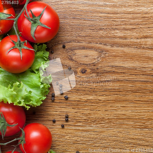 Image of red tomatoes with green salad on wood