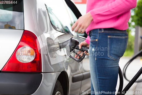 Image of Lady pumping gasoline fuel in car at gas station.