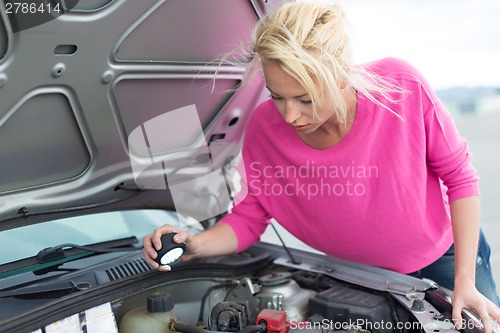 Image of Woman inspecting broken car engine.