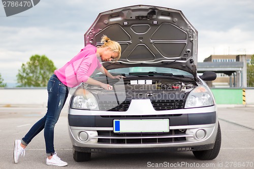 Image of Woman inspecting broken car engine.