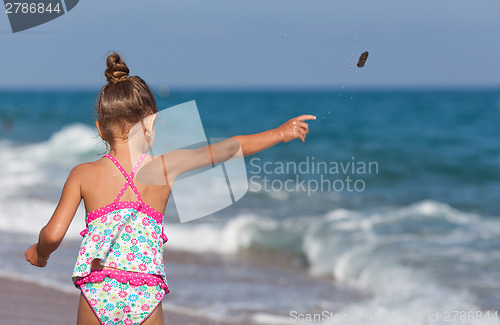 Image of Little girl throws rocks into the sea