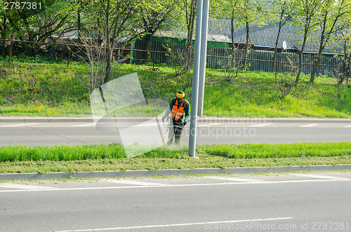 Image of worker with protective mask cuts grass pavement 