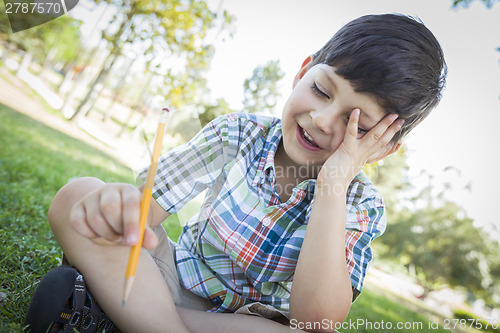 Image of Frustrated Cute Young Boy Holding Pencil Sitting on the Grass