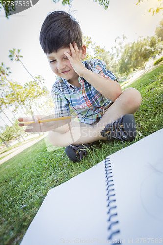 Image of Frustrated Cute Young Boy Holding Pencil Sitting on the Grass