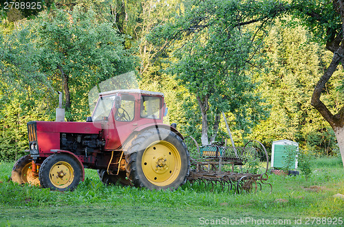 Image of farm tractor with yellow wheels harow in garden  