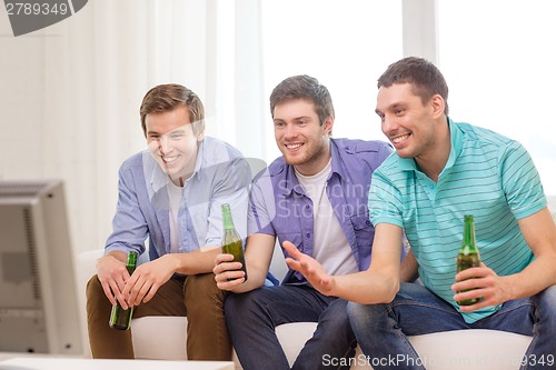 Image of happy male friends with beer watching tv at home